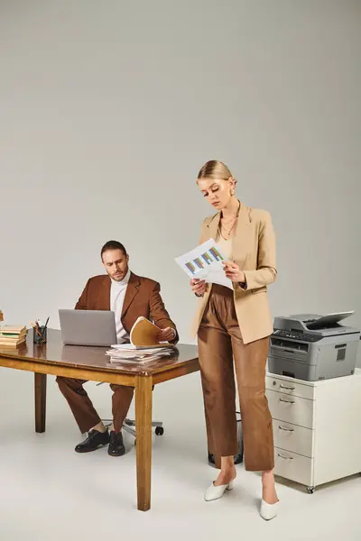 Attractive young woman in stylish attire looking at paperwork while her boyfriend working on laptop — Stock Photo