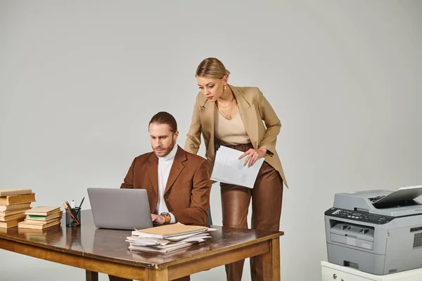 Attrayante femme blonde avec de la paperasse à la main en regardant son petit ami ordinateur portable, affaire de travail — Photo de stock