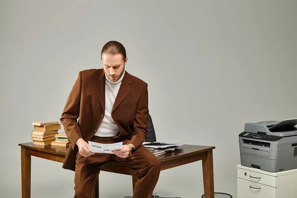 Hombre concentrado bien parecido con barba en chaqueta marrón sentado y mirando su papeleo - foto de stock
