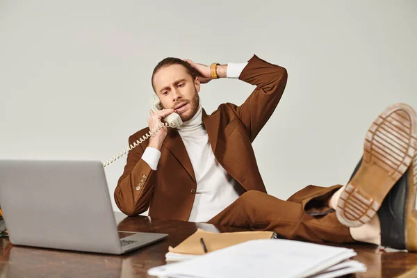 Трудолюбивый элегантный мужчина модель в стильном костюме говорить по старинному телефону с ногами на столе — стоковое фото