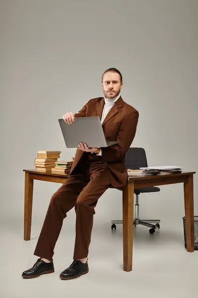 Beau jeune homme avec barbe en brun veste élégante tenant ordinateur portable et regardant la caméra — Photo de stock