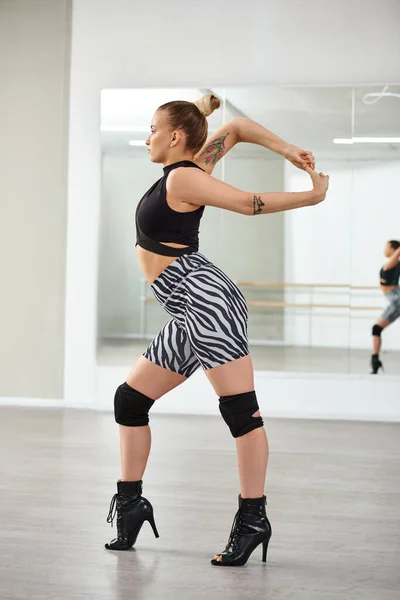 Una bailarina elegante en pantalones cortos de cebra y tacones altos estirándose contra la pared con espejo, coreografía - foto de stock