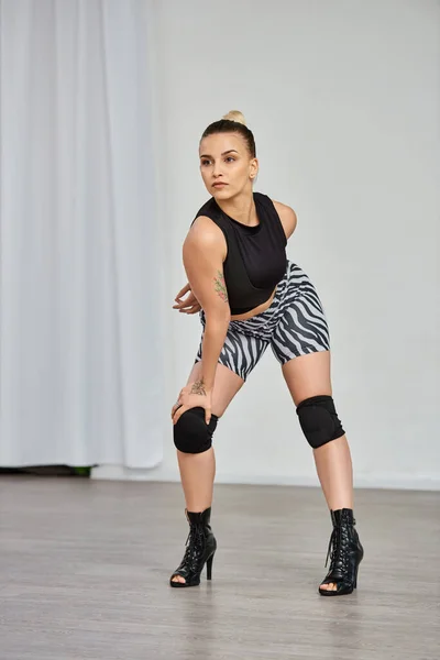 Die gleichgewichtige und anmutige Tänzerin posiert und zeigt Bewegungen in High Heels gegen die weiße Wand — Stockfoto