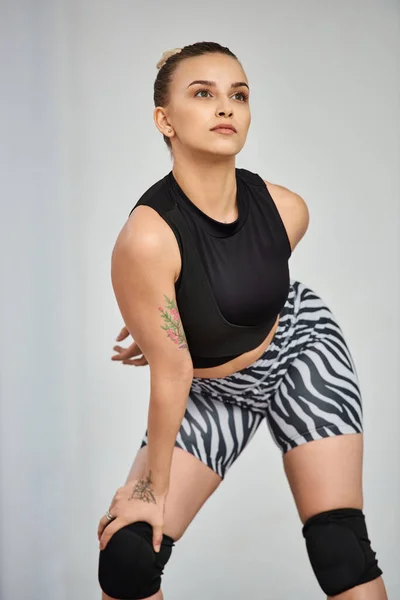 A confident woman in black tank top and zebra shorts balances on one knee, choreography movement — Stock Photo