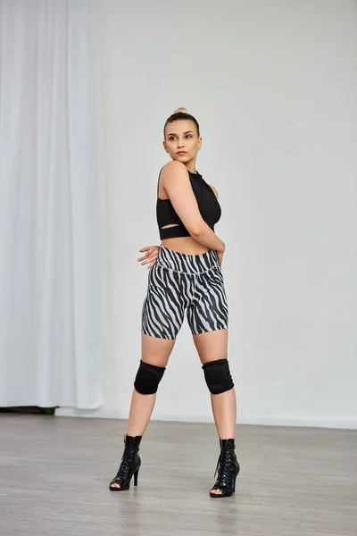 Uma mulher elegante vestindo um top preto e shorts zebra fica em saltos altos contra a parede branca — Fotografia de Stock