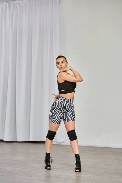 Dancer in high heels and zebra-print shorts dances against white wall, showing off her confidence — Stock Photo