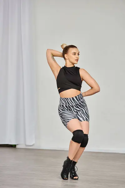 Uma mulher elegante vestindo calções de zebra e top preto dança graciosamente contra uma parede interior — Fotografia de Stock