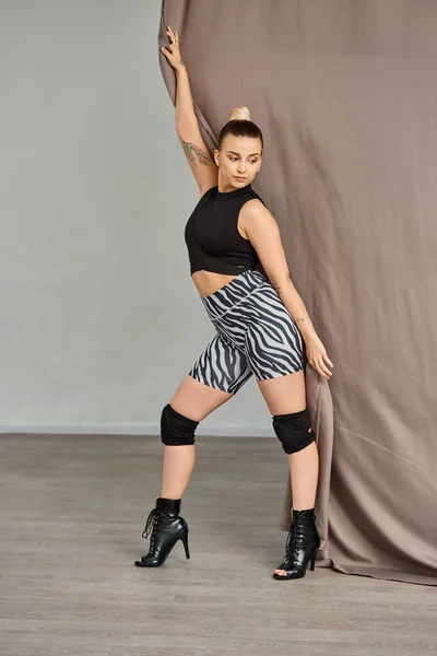 Танцовщица ставит позу в изящном танцевальном движении, балансируя на одной ноге против стены, покрытой занавесом — стоковое фото