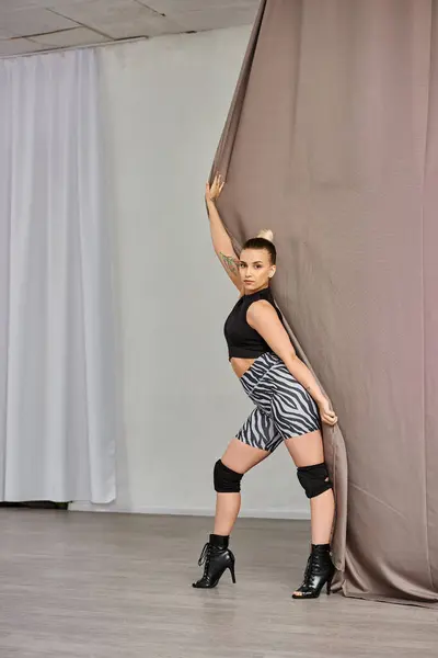 Femme frappe une pose dans le mouvement de danse gracieuse, équilibrant sur un pied contre un mur recouvert de rideau — Photo de stock