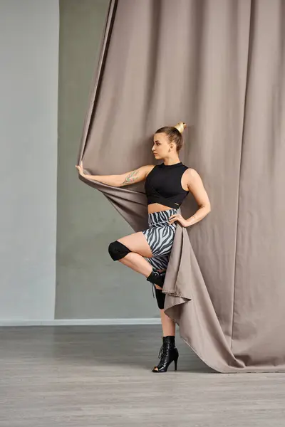Mujer golpea una pose en un elegante movimiento de baile, balanceándose sobre un pie contra una pared cubierta de cortina - foto de stock