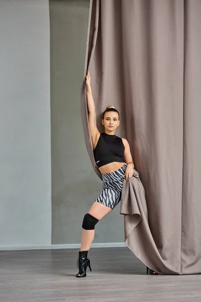 Mulher expressiva em roupas de dança e saltos altos graciosamente posa perto da cortina — Fotografia de Stock