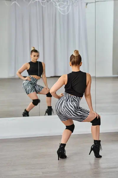 Stylische Frau in Zebra-Shorts und schwarzem Top bewegt sich anmutig auf der Tanzfläche und blickt in den Spiegel — Stockfoto