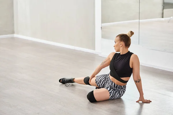 Уравновешенная женщина на высоких каблуках изящно балансирует на одном колене, сидя на танцполе — стоковое фото