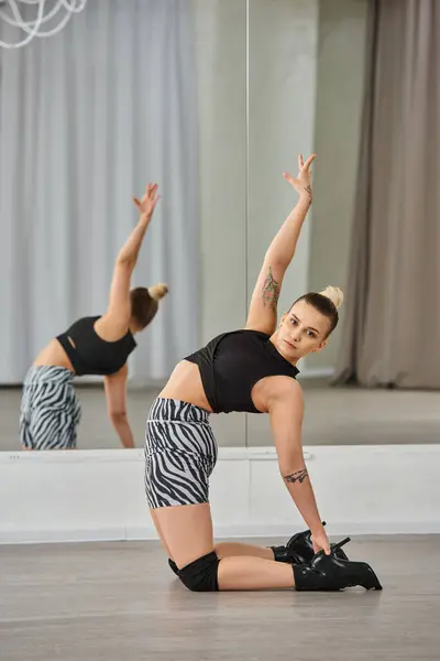 Изящный танцор в зебровых шортах и каблуках растягивает тело возле зеркала в танцевальной студии, хореография — стоковое фото
