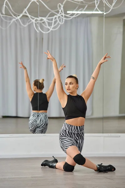 Una graziosa ballerina in tacchi alti e abbigliamento attivo in bianco e nero, si bilancia con grazia su un ginocchio — Foto stock