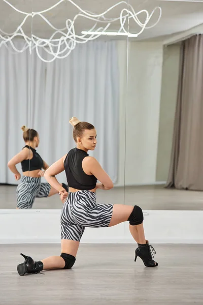 Eine anmutige Tänzerin in High Heels, Shorts mit Zebramuster und schwarzem Oberteil streckt sich vor dem Spiegel — Stockfoto