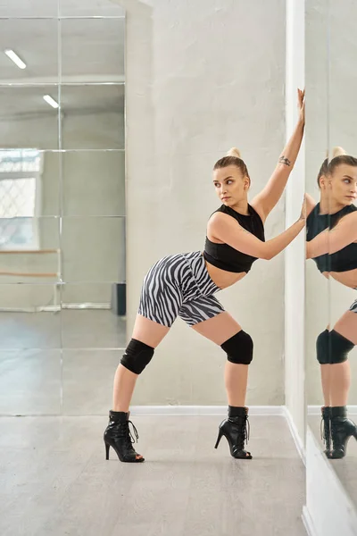Uma gracefulwoman em shorts de zebra e equilíbrio superior preto em uma perna enquanto dança contra o espelho — Fotografia de Stock