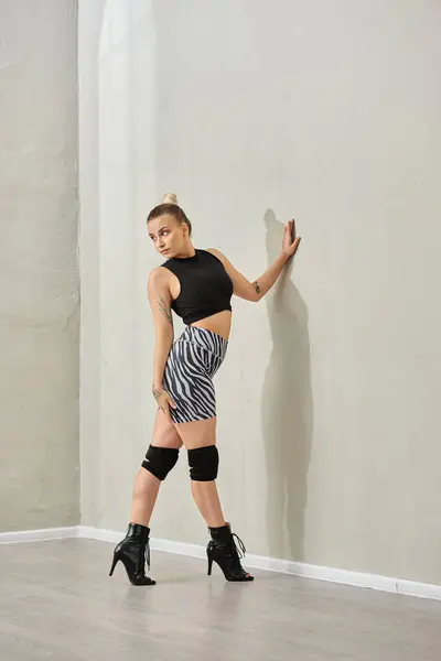 A skilled dancer glides gracefully along the indoor wall, as she confidently posing in high heels — Stock Photo