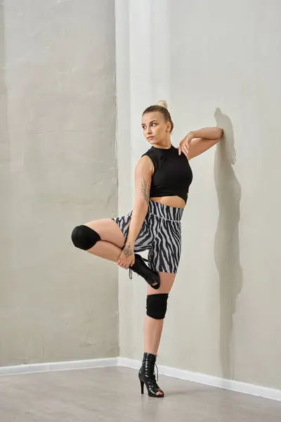 Женщина балансирует на одной ноге против стены, черной верхней и зебры шорты акцентируя ее тонизированные мышцы — стоковое фото