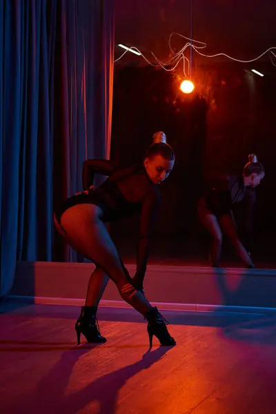 Una bailarina elegante en leotardo negro y medias de rejilla se inclina en una actuación de coreografía - foto de stock