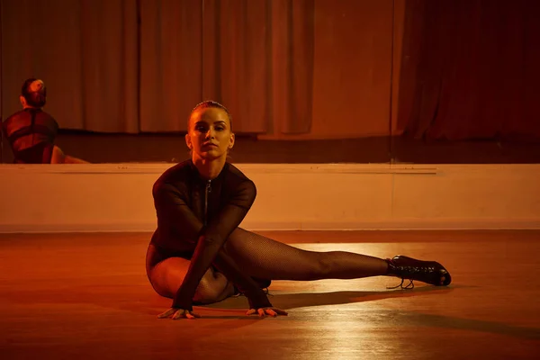 Eine talentierte Tänzerin in High Heels sitzt anmutig auf der Tanzfläche im Studio, fesselnde Szene — Stockfoto