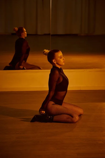 Reflexão no espelho da jovem mulher em roupas pretas e saltos altos sentado na pista de dança — Fotografia de Stock