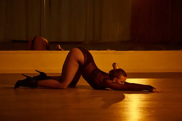 Una mujer elegante en tacones altos estirando su cuerpo sobre el piso pulido en el estudio de baile - foto de stock
