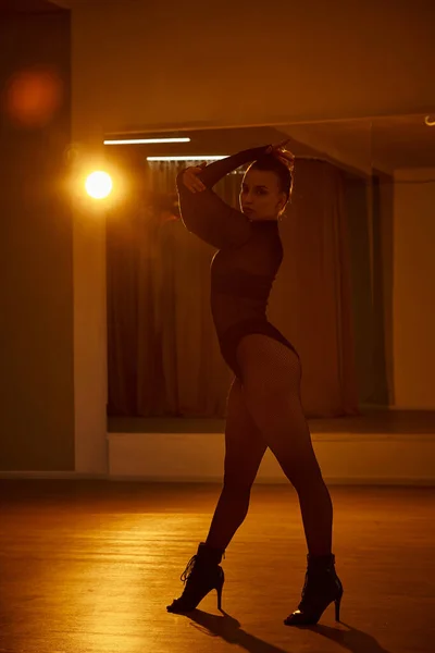 Eine hinreißende Tänzerin in schwarzem Trikot und Netzstrumpfhose bewegt sich anmutig gegen die Wand — Stockfoto