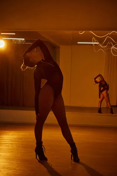 Eine anmutige Tänzerin in schwarzem Trikot und Netzstrumpfhose bewegt sich fließend über den Hallenboden — Stockfoto