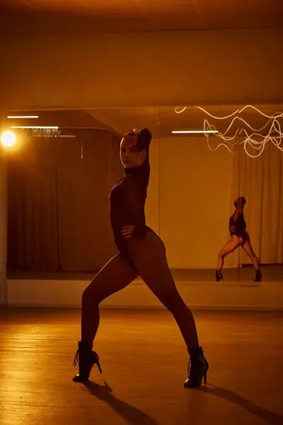 Eine balancierte Frau in Netzstrumpfhose und schwarzem Trikot tanzt auf der Tanzfläche vor einem Studiospiegel — Stockfoto