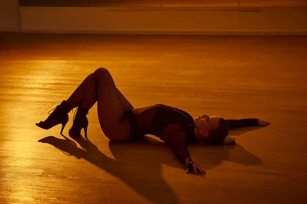 Une danseuse gracieuse trouve son équilibre sur le sol, ses talons hauts touchant le sol du studio — Photo de stock
