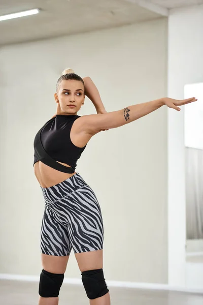 Uma dançarina graciosa estende seu corpo e braços em shorts zebra vibrantes e um top preto, flexibilidade — Fotografia de Stock