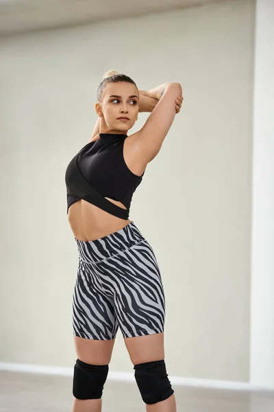 Una bailarina feroz y flexible estira su cuerpo y rms en vibrantes pantalones cortos de cebra y un top negro - foto de stock