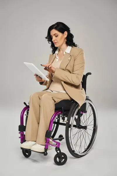 Хороша жінка з обмеженими можливостями в елегантному одязі, сидячи в інвалідному кріслі і дивлячись на її планшет — стокове фото