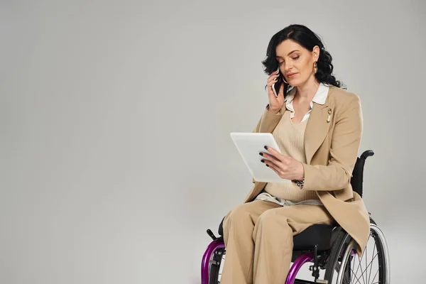 Mujer segura de sí misma con discapacidad al mirar la tableta y hablar por teléfono mientras está en silla de ruedas - foto de stock