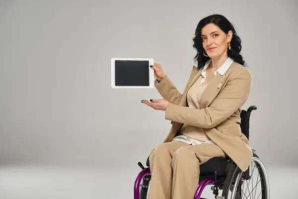 Mulher deficiente atraente em terno elegante sentado em cadeira de rodas e mostrando seu tablet na câmera — Fotografia de Stock
