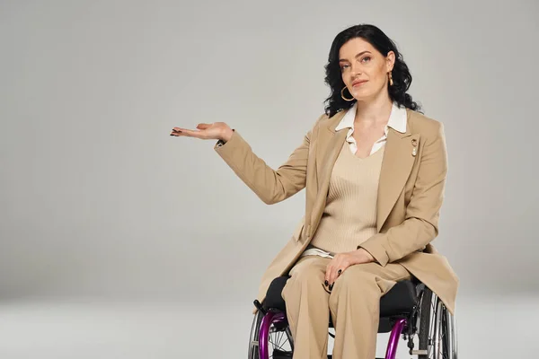 Belle femme handicapée en fauteuil roulant en costume pastel gestuelle et regardant la caméra — Photo de stock