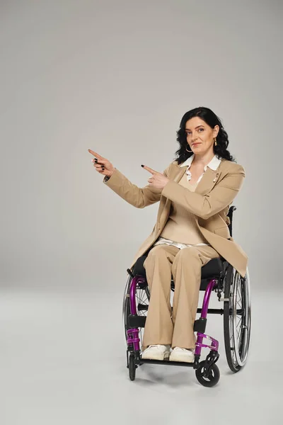 Mujer de buen aspecto con discapacidad capacidad sentado en silla de ruedas y el gesto, mirando a la cámara - foto de stock