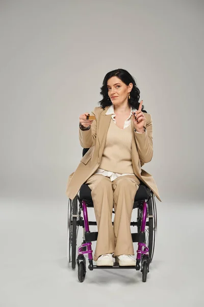 Attrayant femme handicapée assis dans son fauteuil roulant avec carte de crédit et gestuelle activement — Photo de stock