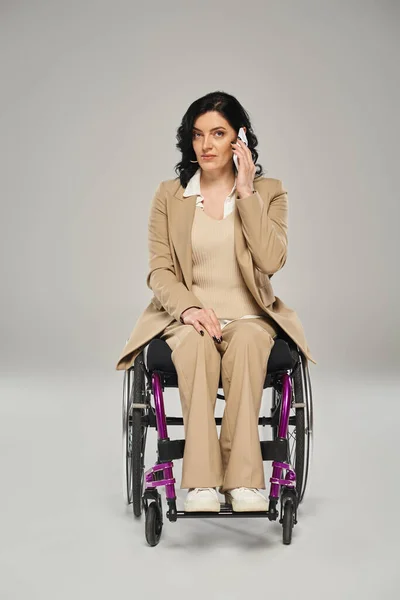 Atractiva mujer con discapacidad en su silla de ruedas y hablando por teléfono, mirando a la cámara - foto de stock
