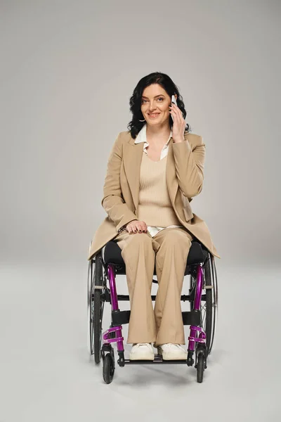 Alegre atractiva mujer con discapacidad en silla de ruedas hablando por teléfono y mirando a la cámara - foto de stock