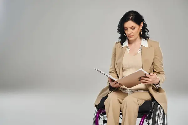 Mujer segura de buen aspecto con discapacidad mirando su papeleo mientras está sentada en silla de ruedas - foto de stock