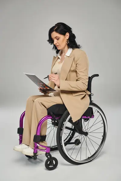 Mujer confiada discapacitada en traje elegante sentada en silla de ruedas y trabajando en sus gráficos - foto de stock