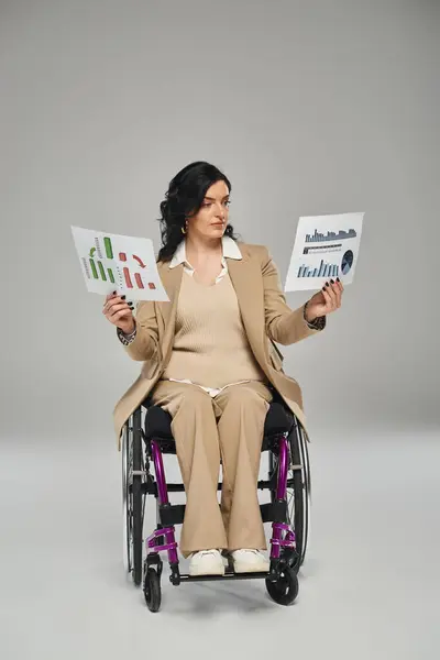 Femme confiante avec un handicap de mobilité en costume chic en fauteuil roulant en regardant ses graphiques — Photo de stock
