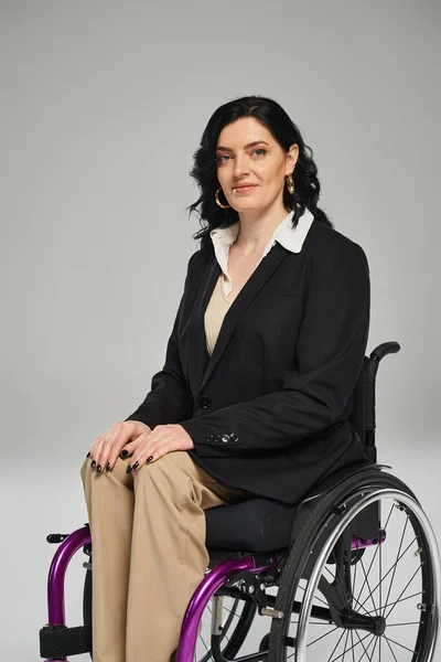 Gai attrayant handicapé femme en noir chic blazer assis en fauteuil roulant et souriant à la caméra — Photo de stock