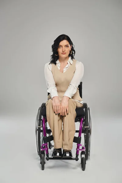 Hermosa mujer discapacitada en pastel elegante traje sentado en silla de ruedas y mirando a la cámara - foto de stock