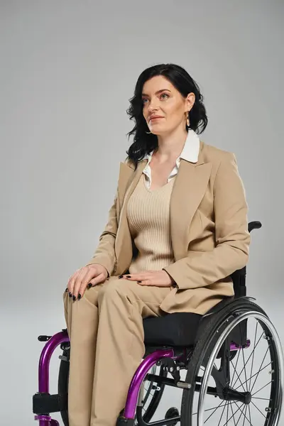 Femme brune confiante avec un handicap en tenue pastel assis en fauteuil roulant et regardant ailleurs — Photo de stock