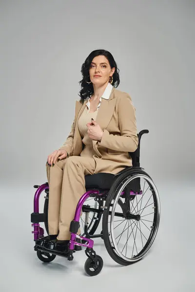 Attrayant brunette femme handicapée en costume élégant assis en fauteuil roulant regardant la caméra — Photo de stock