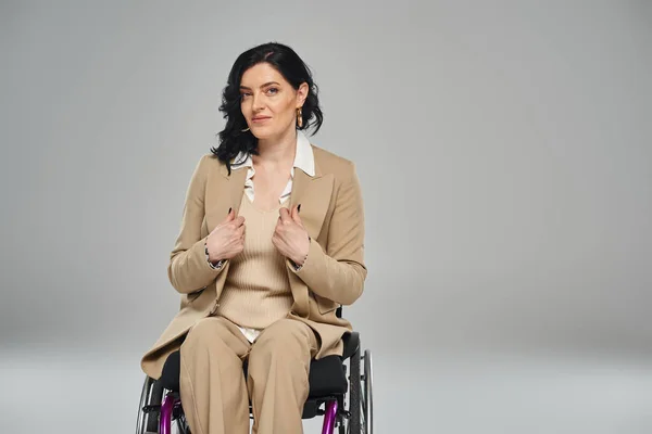 Уверенная в себе женщина с ограниченными возможностями в элегантном костюме пастели сидит в инвалидном кресле и смотрит в камеру — стоковое фото
