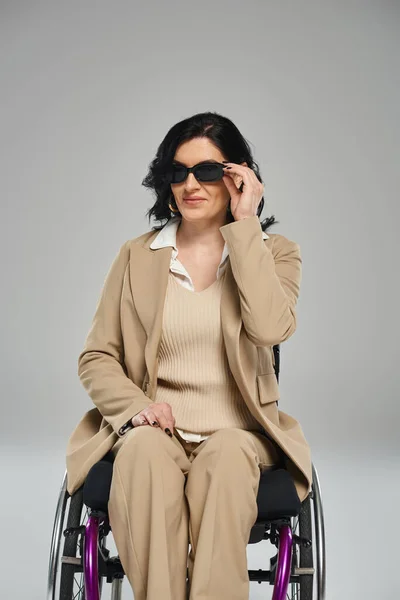 Alegre hermosa mujer con discapacidad en silla de ruedas con gafas de sol y mirando a la cámara - foto de stock